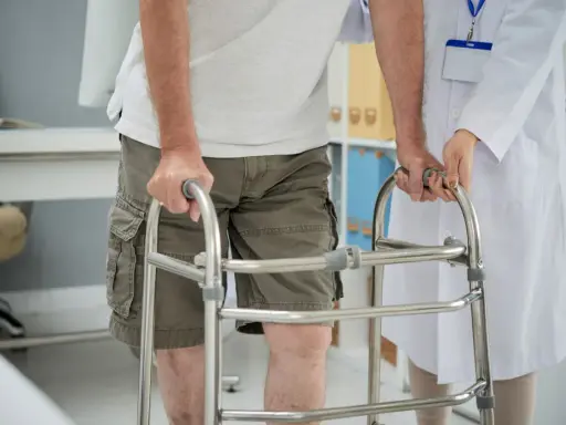 Paziente con problemi di deambulazione che si appoggia a un deambulatore, assistito da un medico.