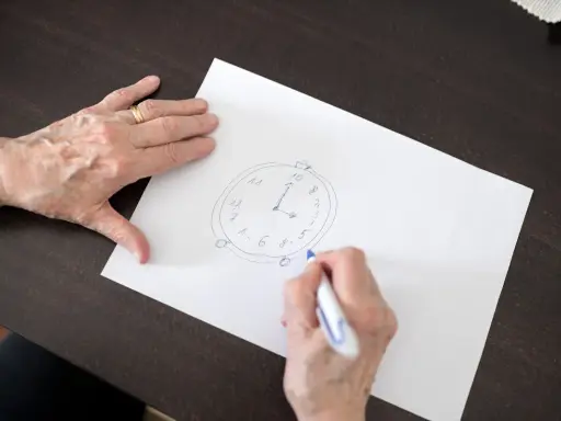 Mani anziane disegnano un orologio su carta, parte di un test memoria anziani.