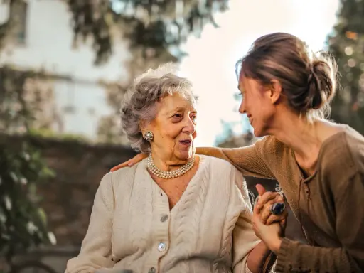 Una donna sorride alla madre anziana, con una mano sulla sua spalla. Finalmente posso portare mia mamma anziana a casa mia.