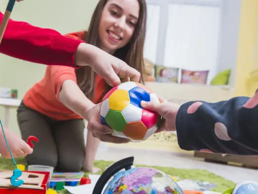 Bambini e terapista giocano con una palla colorata, un globo e un gioco di incastri. La terapia occupazionale cos'è? È questo: gioco e apprendimento.