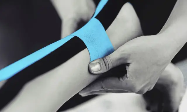 Applicazione di nastro kinesiologico blu e nero per supportare il tendine d'Achille.