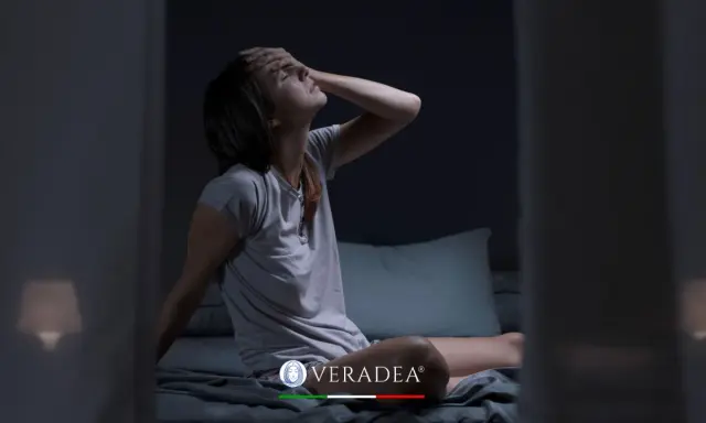 Donna sveglia di soprassalto nel letto, con la mano sulla fronte, soffre di sudorazione notturna. Cerca rimedi per dormire serenamente.