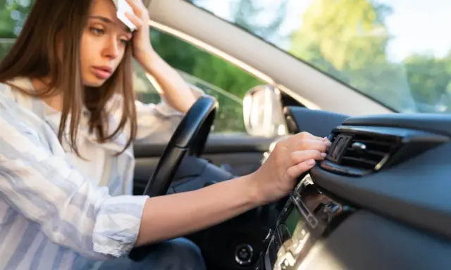 Donna in auto, con un fazzoletto sulla fronte, soffre di sudorazione eccessiva al minimo sforzo, cercando sollievo vicino alla bocchetta dell'aria.