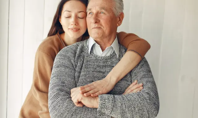 Un abbraccio affettuoso: un modo per come calmare una persona con demenza senile. La giovane donna stringe dolcemente l'anziano uomo, offrendo conforto e sicurezza.