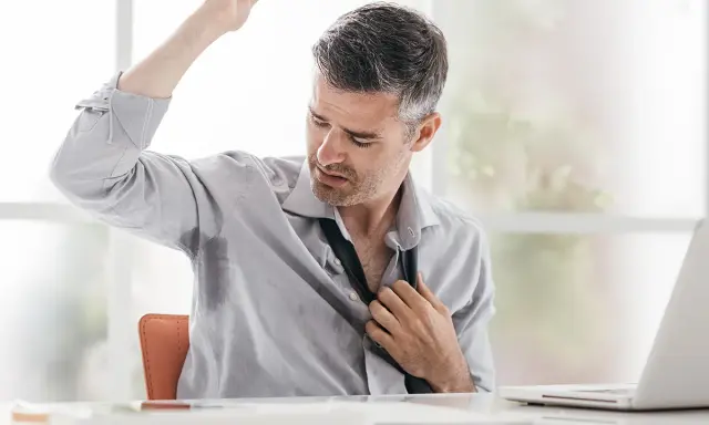 Uomo d'affari con camicia bagnata di sudore sotto le ascelle, che si sbottona la cravatta. Le cause del sudare freddo sono molteplici.
