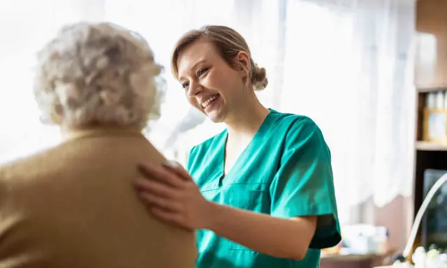 Infermiera sorridente incoraggia un'anziana con difficoltà a parlare, offrendo supporto e comprensione.