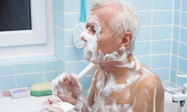 Un anziano con Alzheimer, coperto di schiuma, si lava. Un gesto di cura per convincerlo a lavarsi.