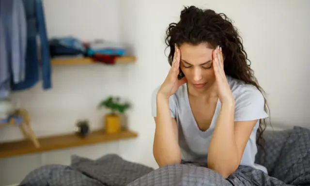 Donna con le mani sulle tempie, seduta a letto, soffre di giramenti di testa.