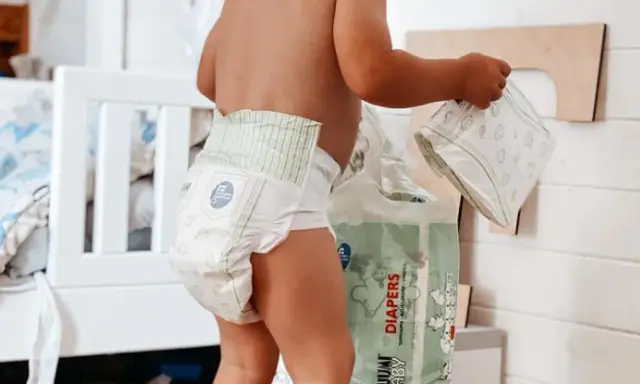 Un bimbo con un pannolino indosso, vicino a una confezione di pannolini. Sembra che i pannolini scadano, ma non c'è fretta.