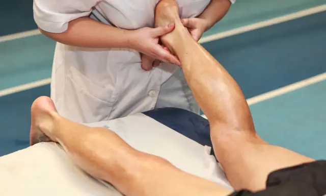 Mani esperte eseguono un massaggio trasverso profondo alla caviglia e al polpaccio di un atleta, alleviando la tensione muscolare.