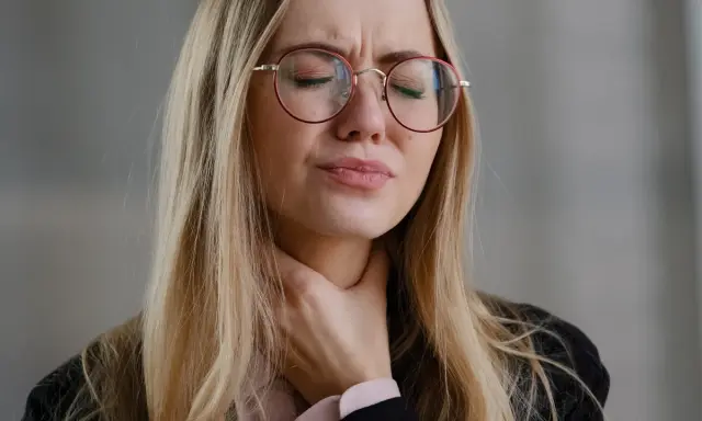 Donna con occhiali rossi si stringe la gola, visibilmente sofferente. Cerca rimedi per un prurito insopportabile.