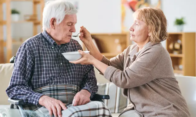 Una donna nutre con un cucchiaino il suo anziano nonno, che non mangia più, seduto su una sedia a rotelle.