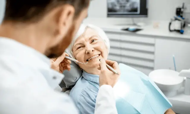Un dentista esamina i denti di un'anziana sorridente, sottolineando l'importanza dell'igiene orale per gli anziani.