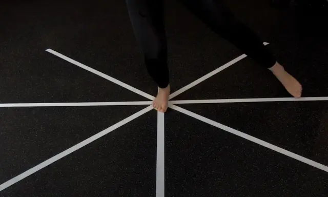 Persona esegue un test di equilibrio su un pavimento con nastro bianco a raggiera.