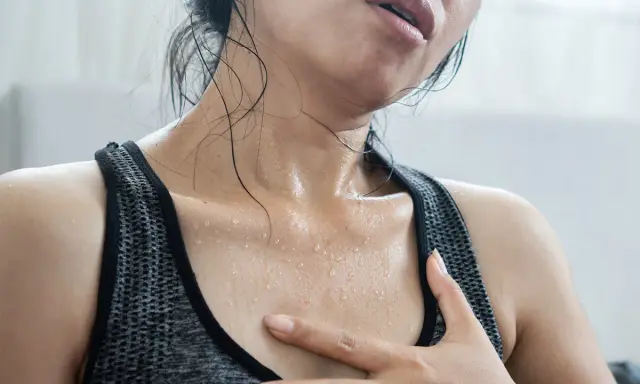 Donna con sudorazione notturna alla stessa ora, visibilmente affaticata, con gocce di sudore sul collo e sul petto.