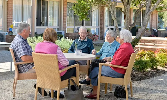Anziani riuniti in giardino, chiacchierano e sorridono. Un momento sereno nella loro casa di riposo RSA.