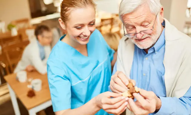 Assistente sorridente aiuta un anziano con demenza a completare un puzzle, mostrando come le fissazioni possano essere gestite con pazienza e attività stimolanti.