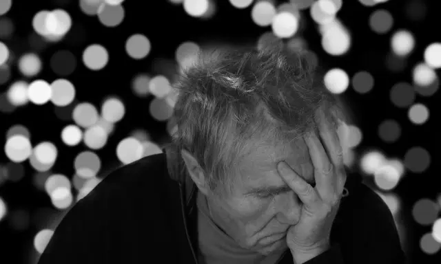 Uomo anziano con mano sulla fronte, pensieroso. L'Alzheimer può manifestarsi a diverse età, ma è più comune dopo i 65 anni.