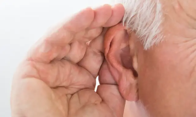 Mano di anziano che copre l'orecchio, forse per sentire meglio o per proteggersi da allucinazioni uditive.