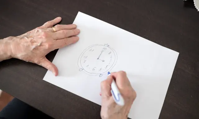 Mani anziane disegnano un orologio su carta, parte di un test memoria anziani.