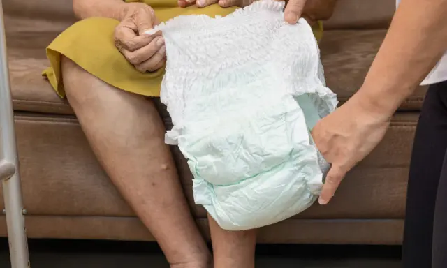 Mani che mostrano come si mette il pannolino a un'anziana seduta.