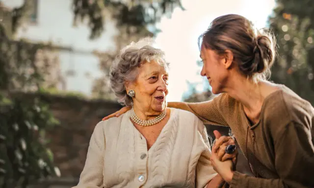 Una donna sorride alla madre anziana, con una mano sulla sua spalla. Finalmente posso portare mia mamma anziana a casa mia.