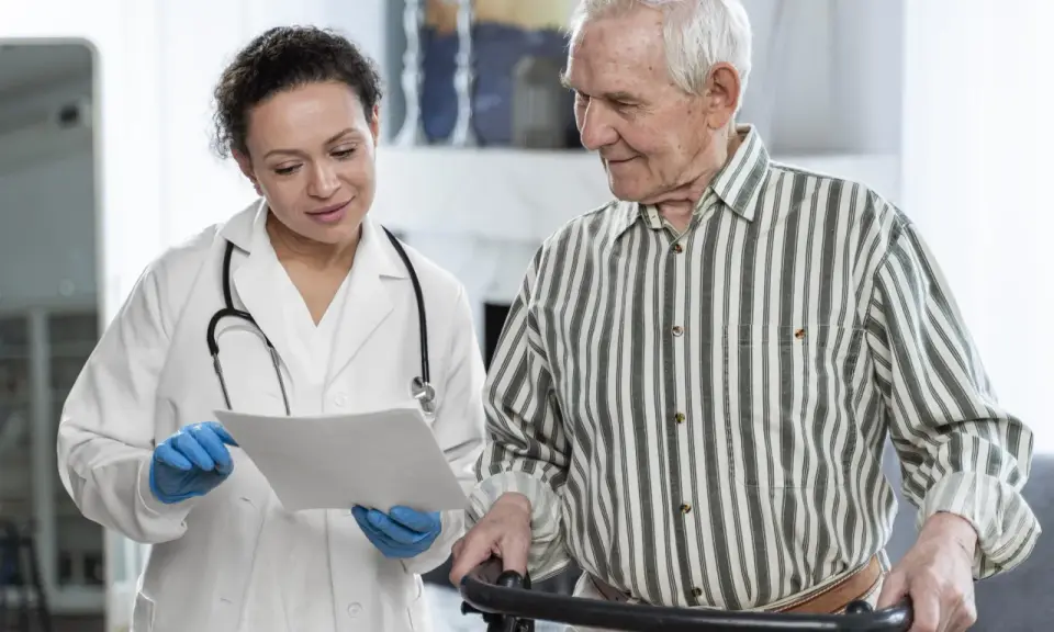 Medico spiega a paziente anziano con deambulatore il significato di un problema cognitivo, mostrando un documento.