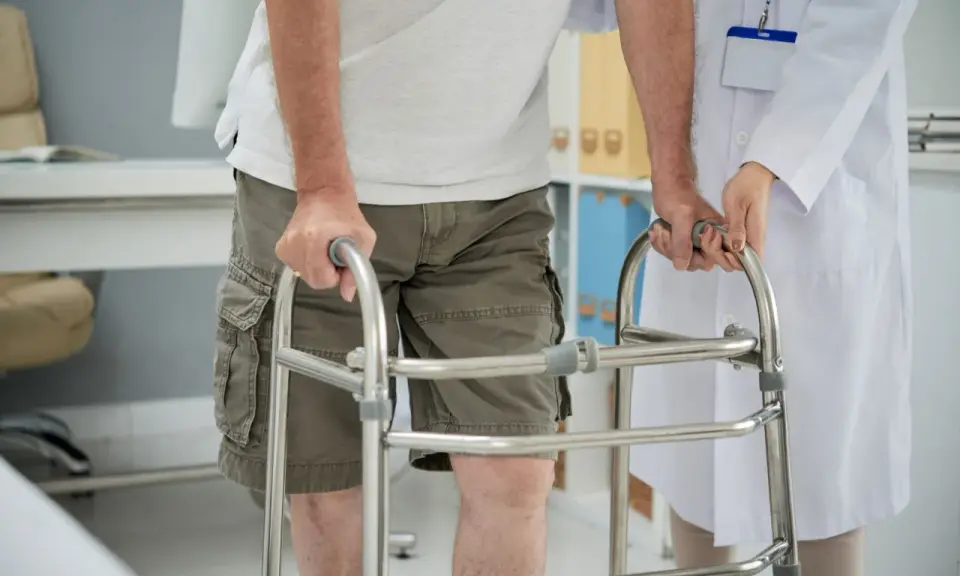 Paziente con problemi di deambulazione che si appoggia a un deambulatore, assistito da un medico.