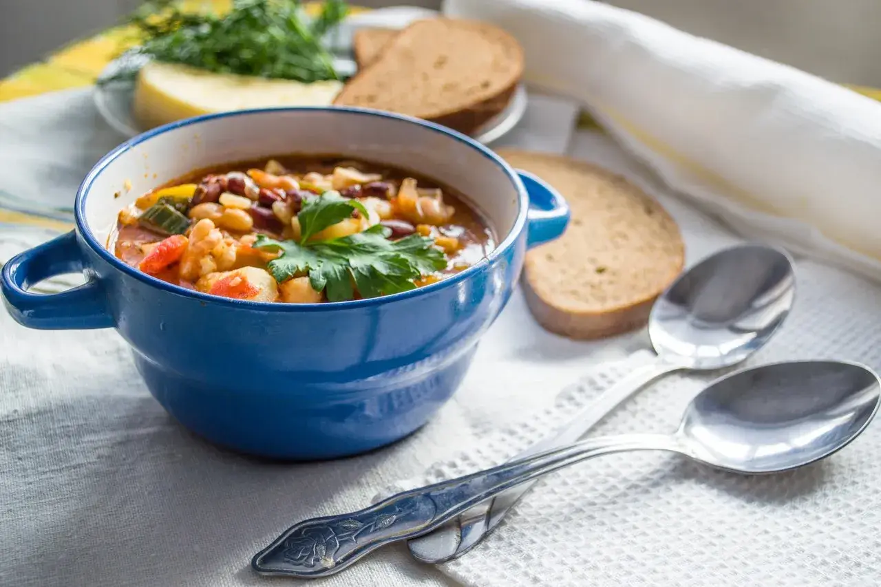 Zuppa nutriente, ideale per una dieta per anziani over 90. Servita in ciotola blu con pane integrale e erbe fresche.