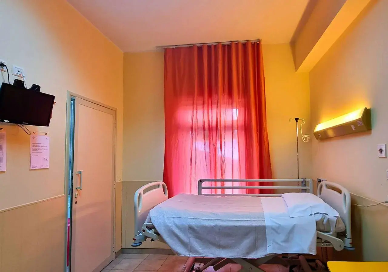Stanza ospedaliera con letto, tenda rossa e TV. Esempi di cure palliative per un comfort sereno.