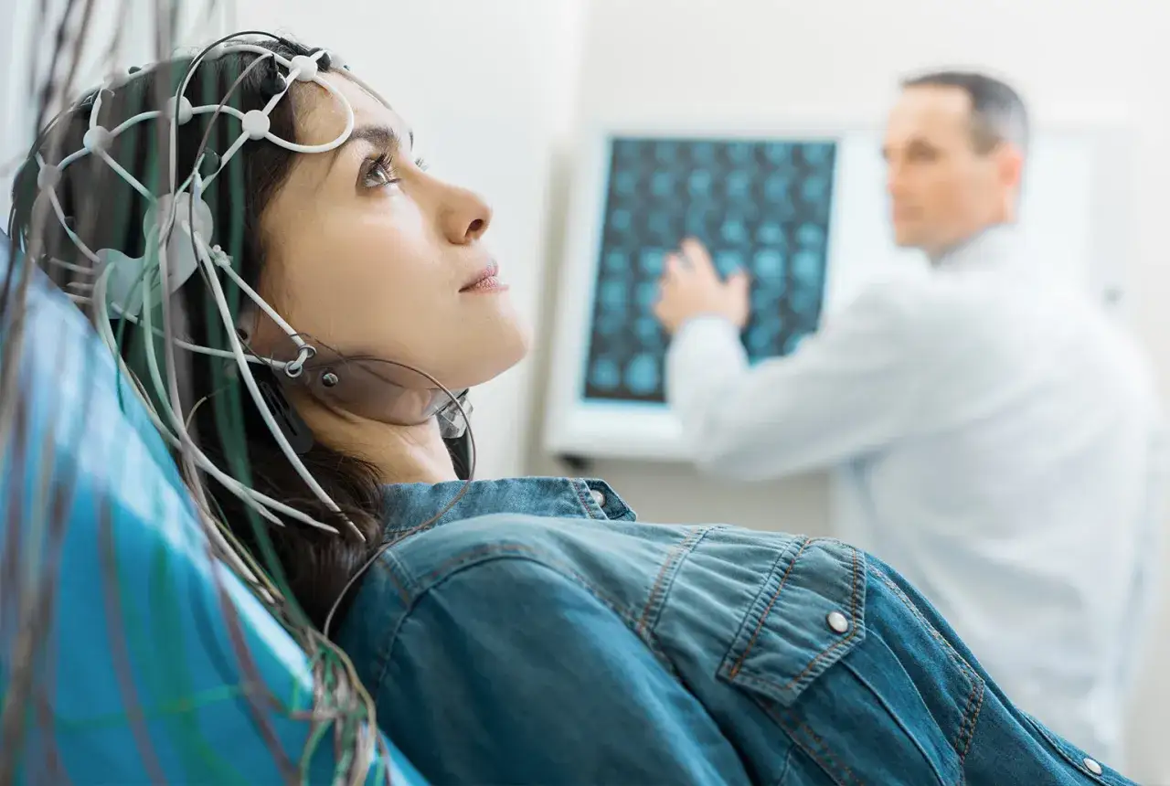 Donna con elettrodi sulla testa per un esame neurologico, mentre un medico osserva una scansione cerebrale.