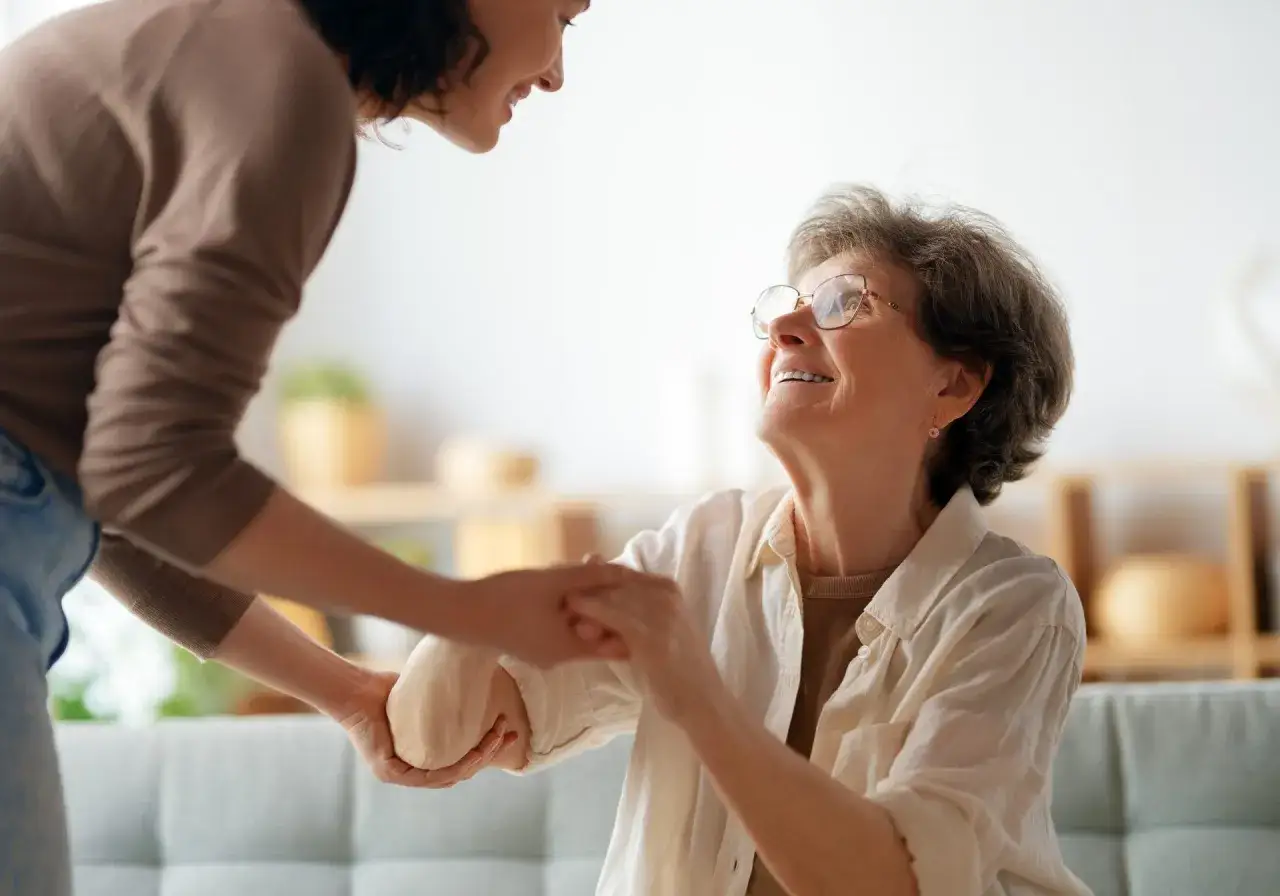 Una giovane donna aiuta un'anziana a rialzarsi. Un gesto di cura che mostra come un caregiver può sopravvivere con amore e supporto.