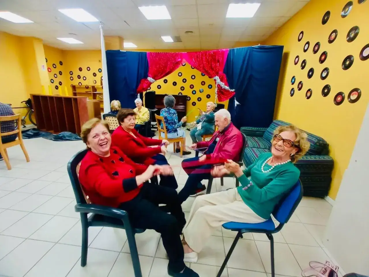 Anziani sorridenti partecipano a iniziative ricreative, con dischi in vinile decorativi alle pareti.
