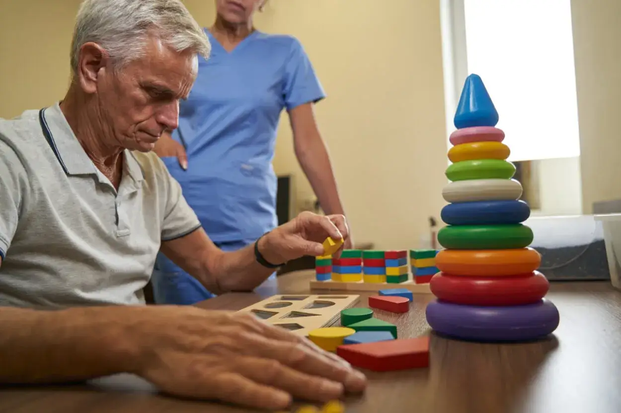 Esempi di terapia occupazionale anziani: un uomo anziano con un terapista gioca con blocchi colorati e un puzzle di forme.