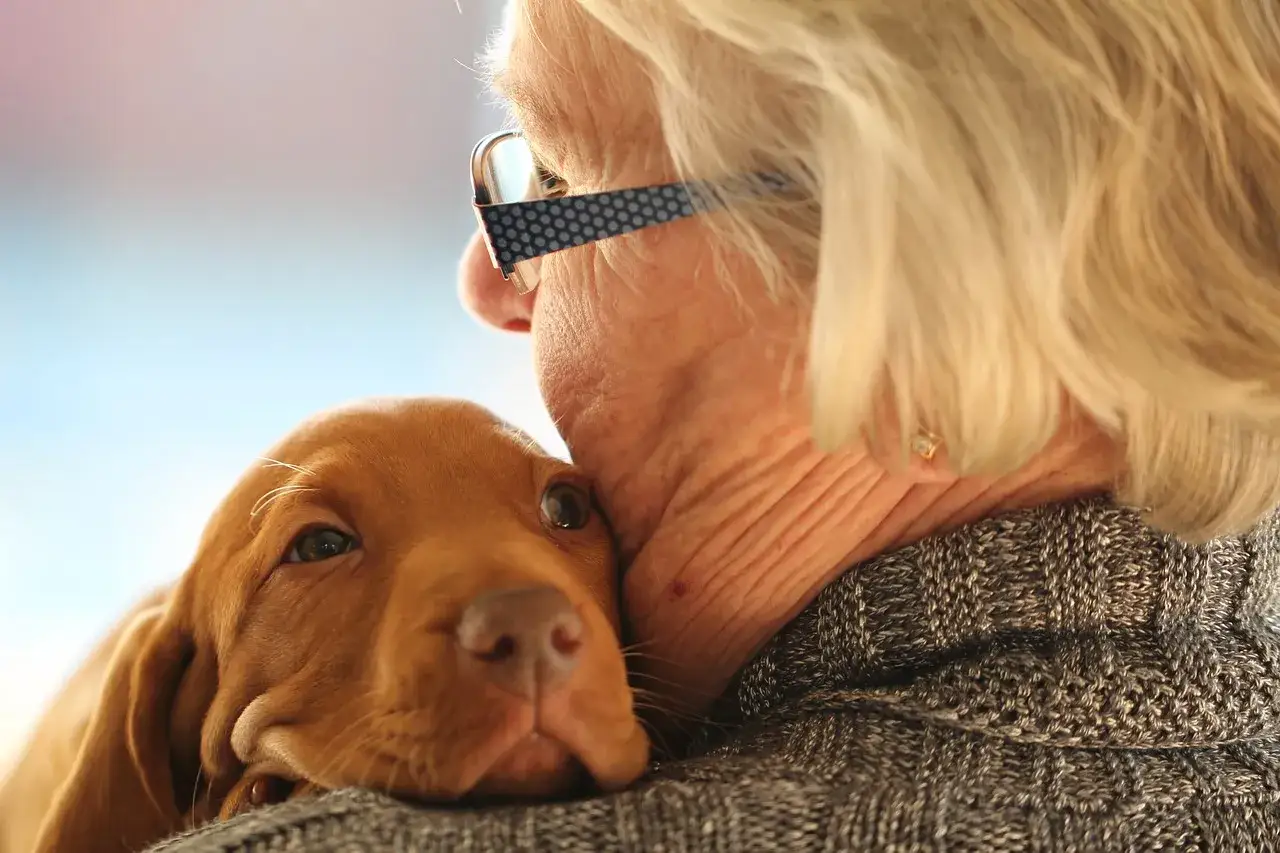 Un cucciolo marrone riposa sul petto di un'anziana con occhiali. Un momento di pura pet therapy anziani.