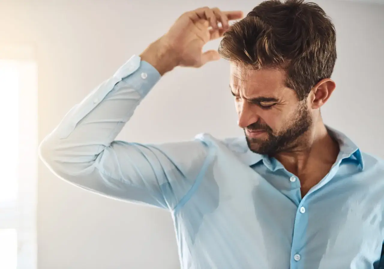 Uomo con camicia azzurra bagnata di sudore sotto le ascelle, preoccupato per la sudorazione eccessiva: cause uomo.