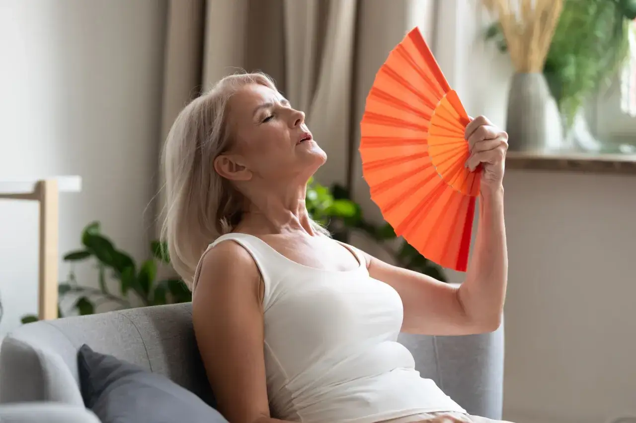 Donna anziana con ventaglio arancione, soffre il caldo. Potrebbe essere un sintomo di sudorazione eccessiva notturna negli anziani cause.