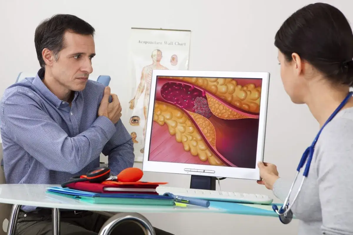 Medico mostra a paziente immagine di arteria ostruita, spiegando la convalescenza dopo coronarografia.