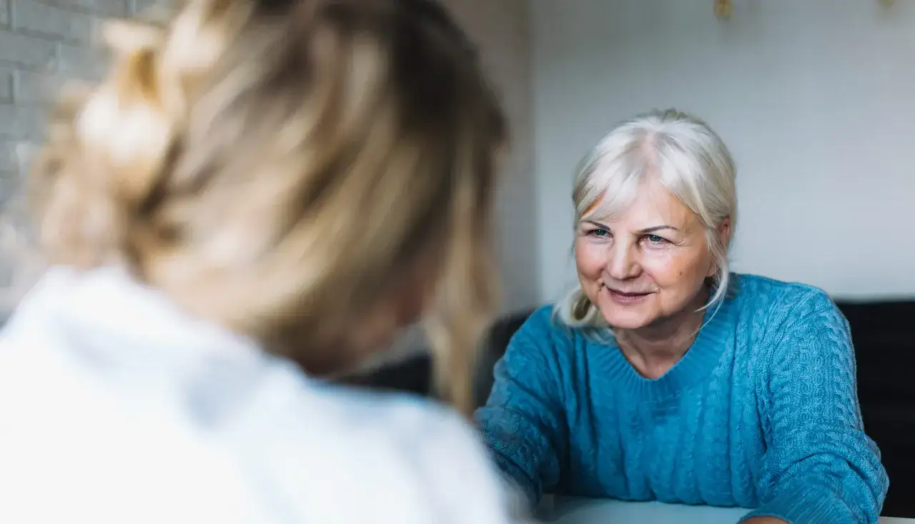 Una donna anziana con capelli biondi guarda con affetto un'altra persona. Un momento di connessione per chi affronta l'Alzheimer, mostrando come comportarsi con empatia.
