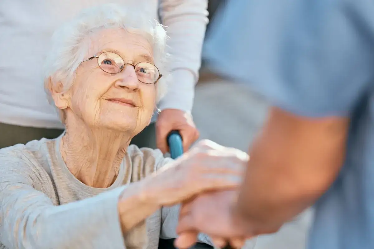 Anziana sorride mentre una mano la tiene. Trovare una badante affidabile è fondamentale per la serenità.
