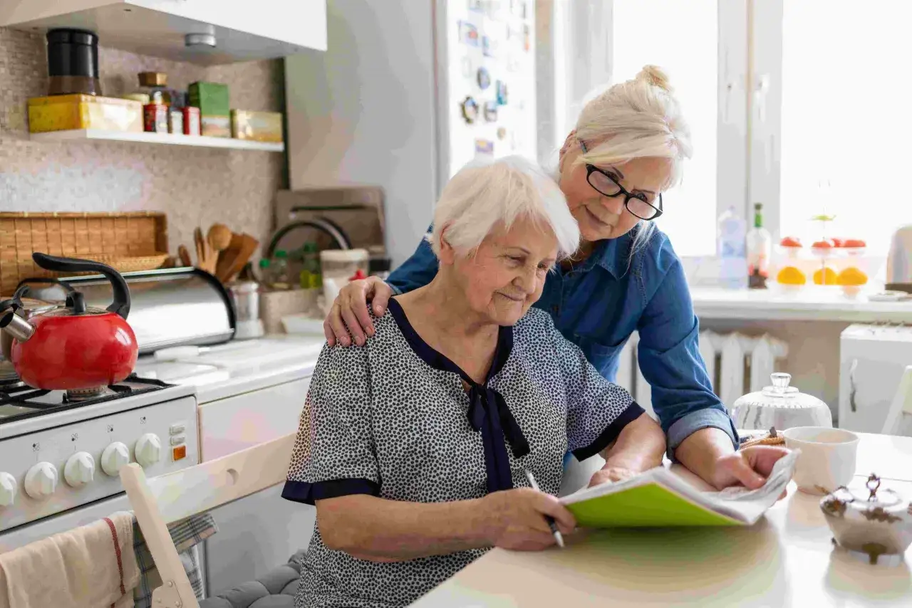 Una donna assiste un'anziana che legge, un momento di cura che può indicare quando ricoverare un malato di Alzheimer, valutando il supporto necessario.
