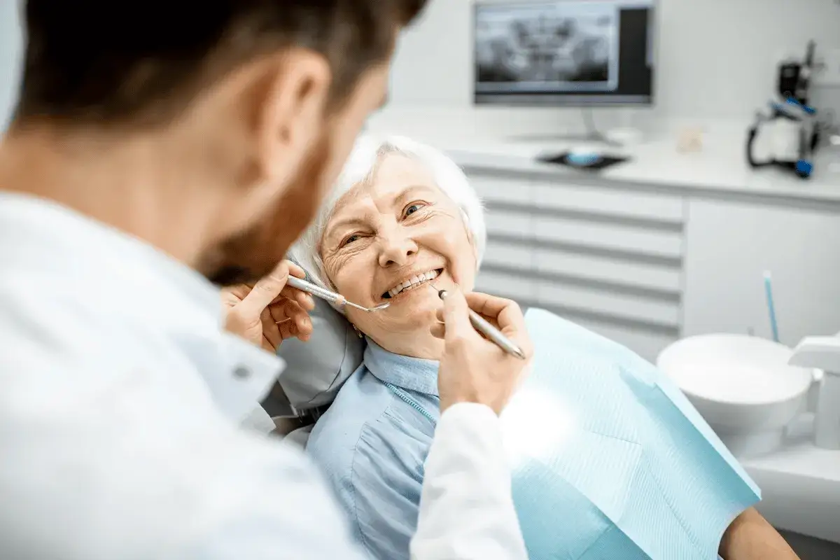 Dentista esamina i denti di un'anziana sorridente, sottolineando l'importanza dell'igiene orale anziani per un sorriso sano.