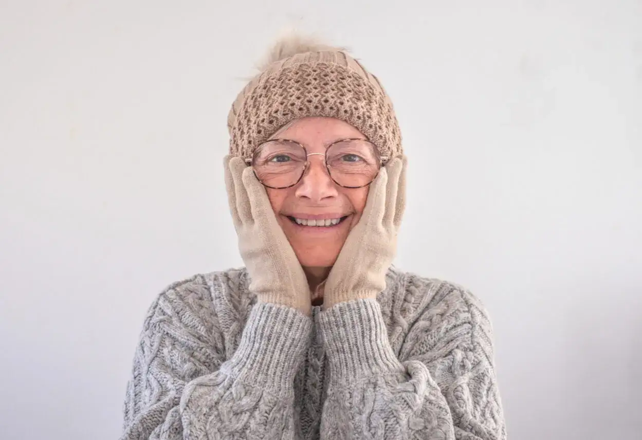 Donna sorridente con cappello e guanti, la sua pelle avvizzita a 65 anni non le impedisce di mostrare gioia.