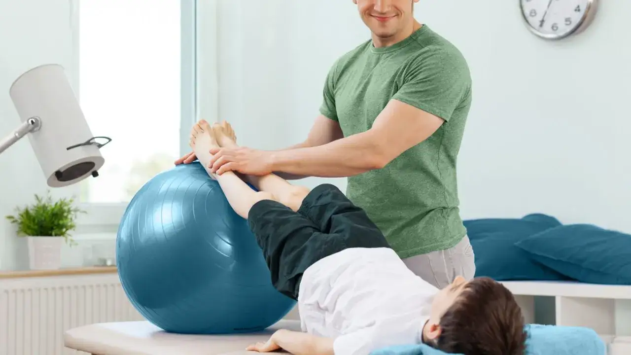 Fisioterapista aiuta un bambino con esercizi su palla, per prevenire il perdere massa muscolare cause.