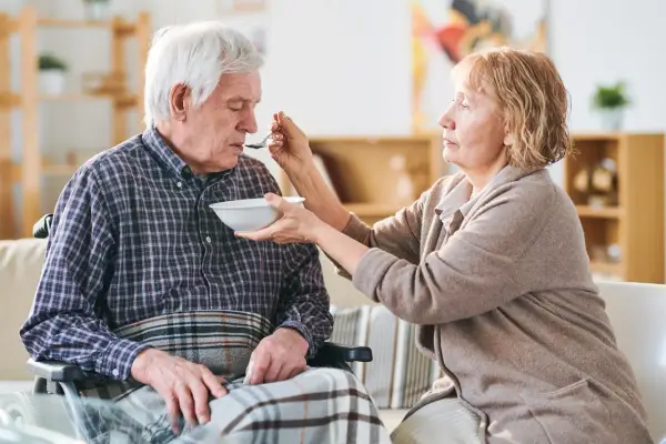 Una donna nutre con un cucchiaino il suo anziano nonno, che non mangia più, seduto su una sedia a rotelle.