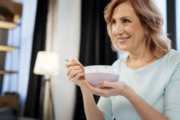 Donna sorride mentre mangia una zuppa cremosa, un esempio di cosa mangiare con disfagia.