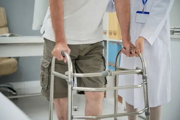 Paziente con problemi di deambulazione che si appoggia a un deambulatore, assistito da un medico.