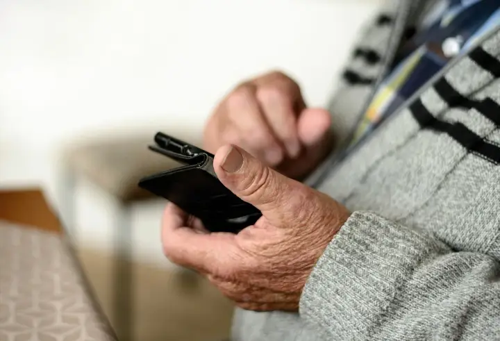 Mani anziane che tengono uno smartphone, forse per capire come fare lo SPID.