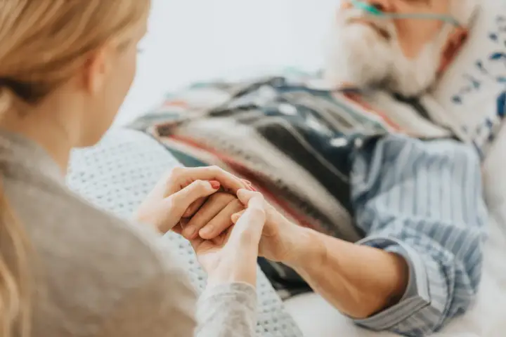 Mani che si stringono tra una giovane donna e un anziano in ospedale. Scopri cosa spetta a chi assiste un familiare con la 104.