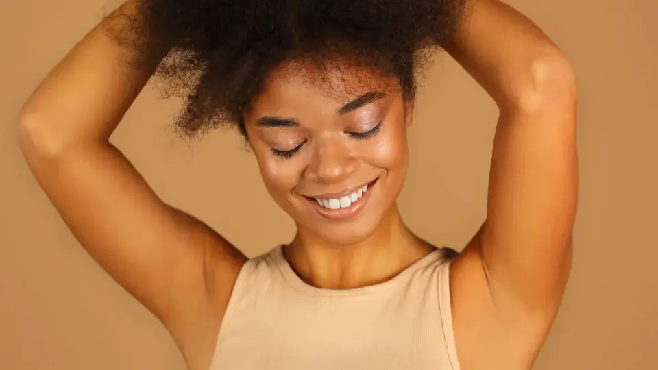 Donna sorridente con le braccia alzate, mostrando le ascelle. Scopri i migliori rimedi naturali per le ascelle irritate.